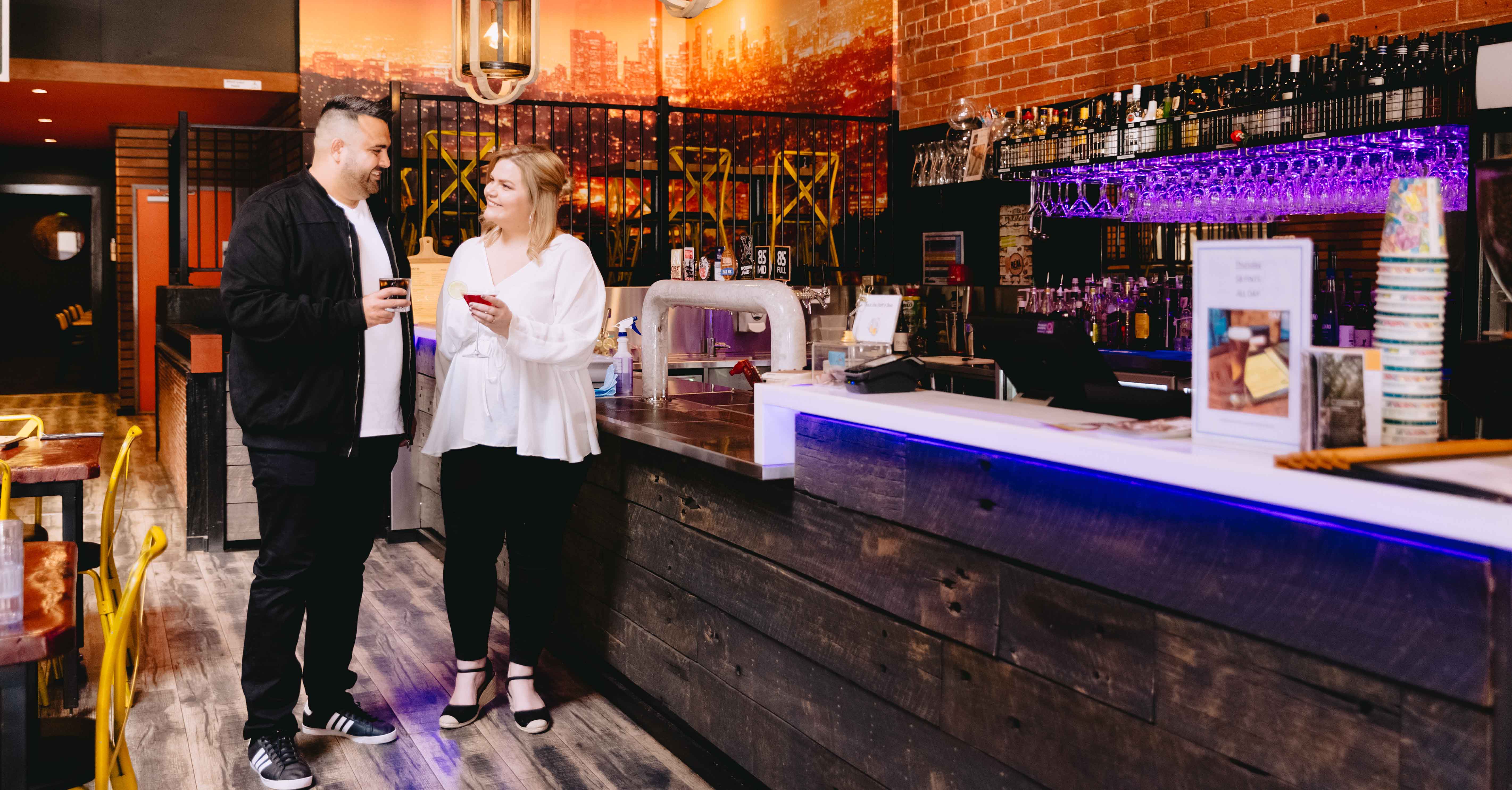 Male and female standing at a bar with drinks 