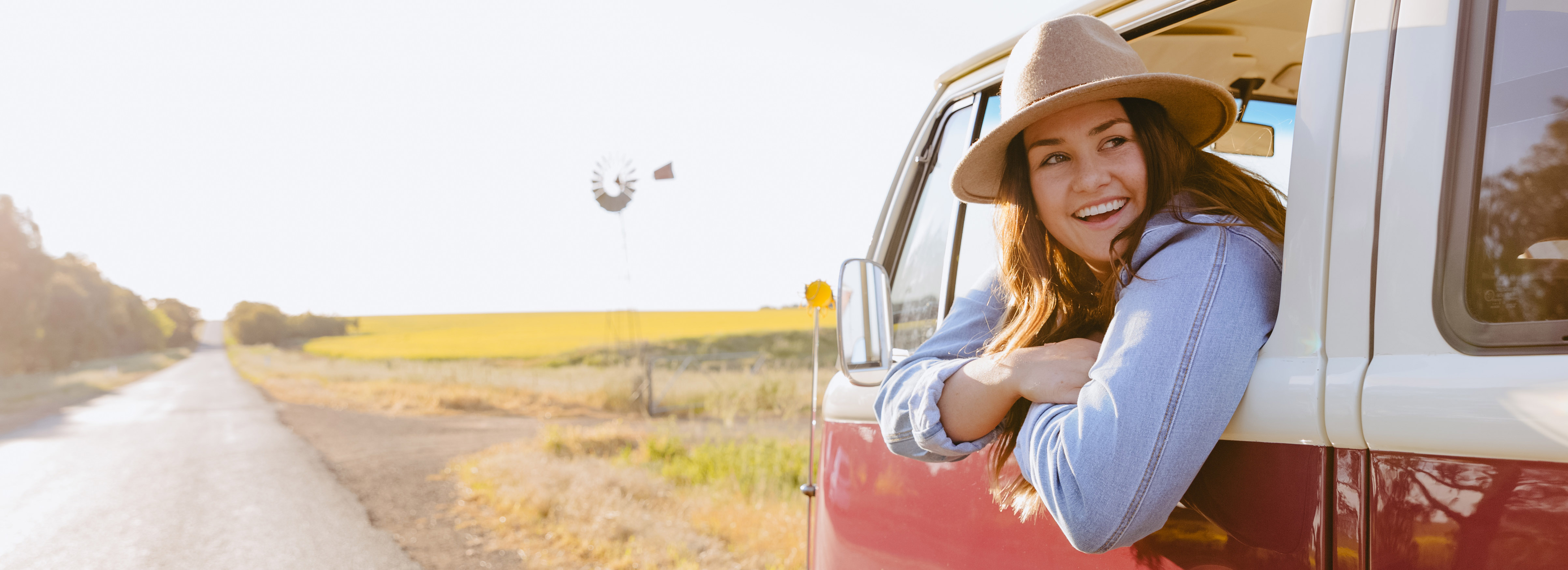 Girl looking out the window of a kombi van with a road beside her disappearing into the distance